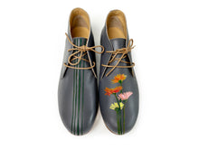 Load image into Gallery viewer, A pair of beige women&#39;s flats with hand-painted flower designs, displayed against a backdrop featuring a woman in a flowered dress.
