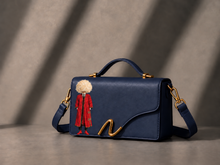 Load image into Gallery viewer, Signature N Turkaman navy leather handbag featuring a figure in a red coat and cream hat
